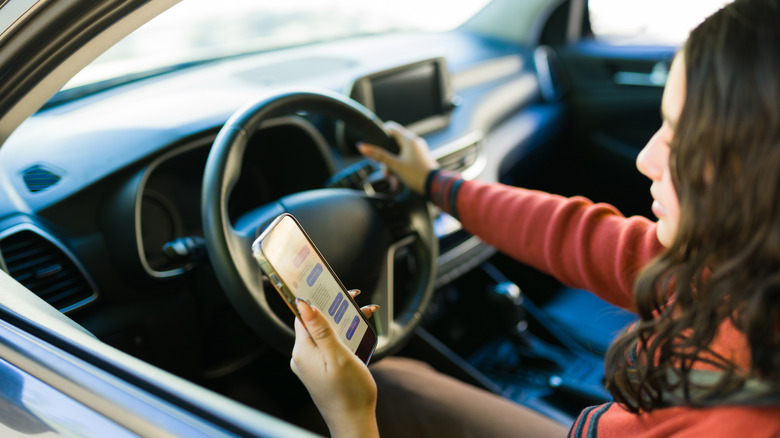 Person using a smartphone will seated in the driving seat of a car