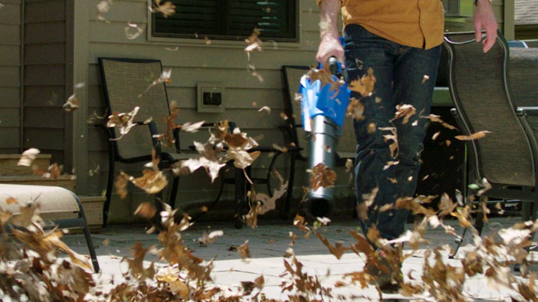 A blue Kobalt blower sends brown leaves fly in the air.