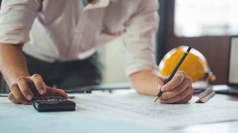 Close-up of a person in business attire working on project plans, a yellow hard hat sitting nearby