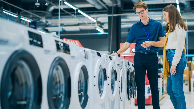 A customer and an employee look at washing machines in a store.