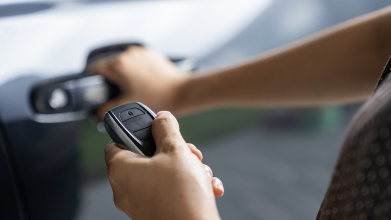 A person holding a key fob while opening a car door.