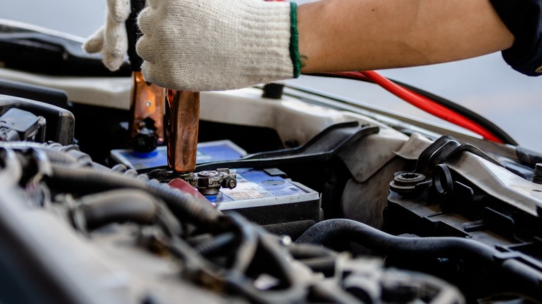 Hands holding jumper cables on car battery