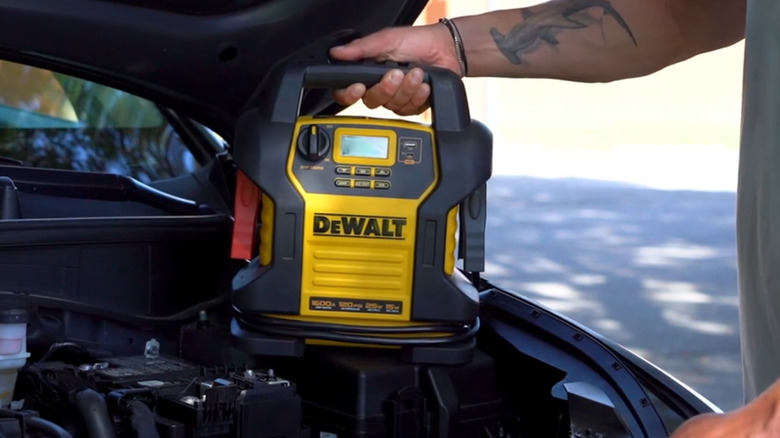 person placing a jump starter in a car's engine bay