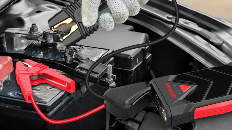 person attaching jump starter clamps to battery