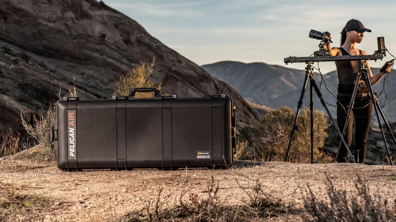 A Pelican Air case on the ground, next to a woman who is using camera gear