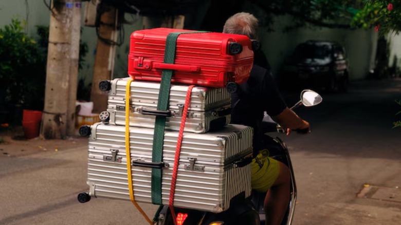 Three Rimowa suitcases balanced on the back of a motorcycle