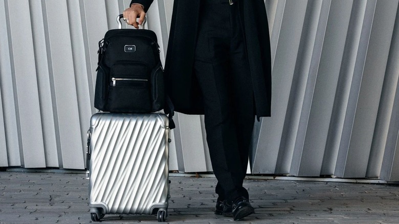 A person standing next to a Tumi suitcase and a backpack
