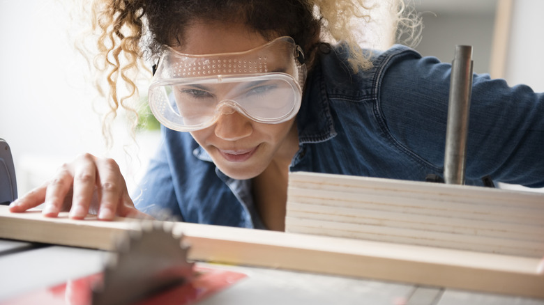 A woman wearing safety glasses prepares to cut a piece of wood with a circular saw.