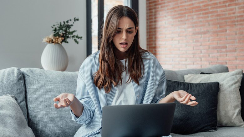 Frustrated woman sits on couch with laptop