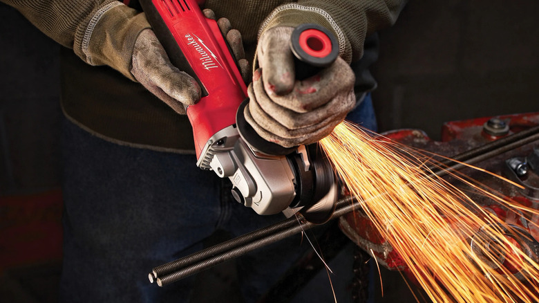 A worker wearing gloves using a Milwaukee angle grinder on metal rods