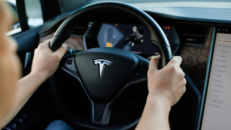 person driving a tesla with hands on teering wheel
