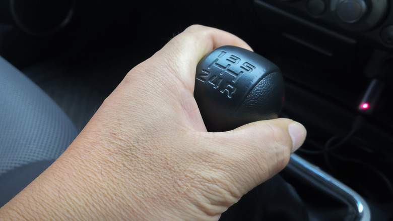 left hand holding the shift knob of five-speed manual car