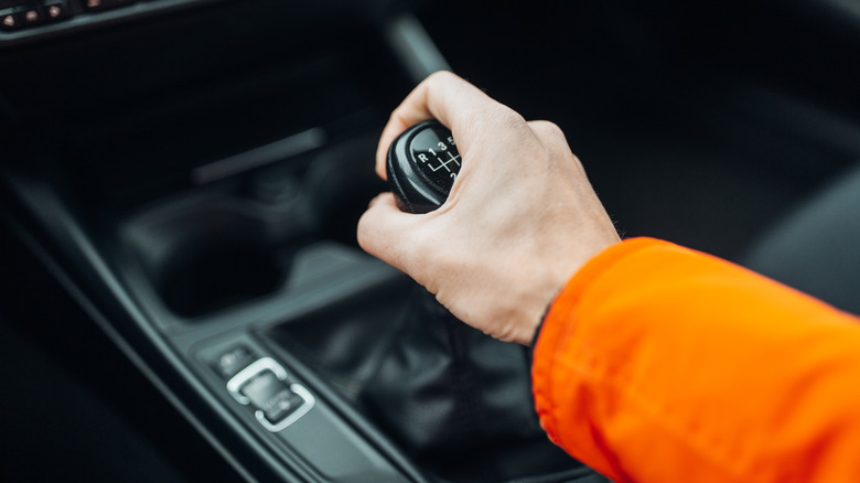 A person holding a manual shift lever in an older BMW