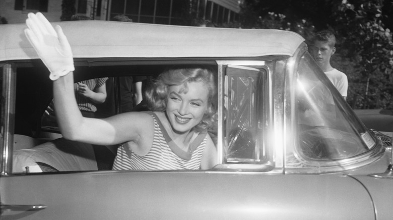 Marilyn Monroe waves from the passenger window of a car