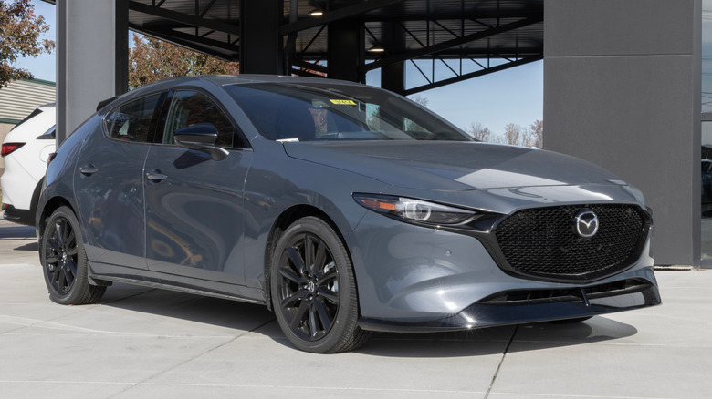 Front 3/4 view of gray Mazda3 hatchback parked in front of dealership.