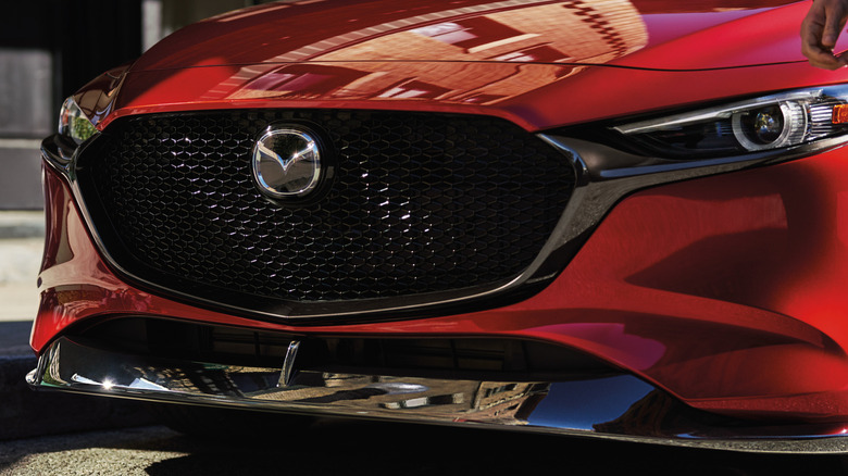 A close-up of the front grille of a red Mazda3, black splitter