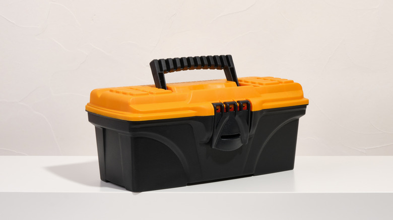 Black plastic tool box with yellow lid sitting in white room