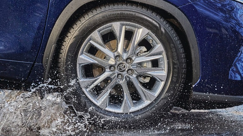 A Goodyear tire on a car driving through a puddle.