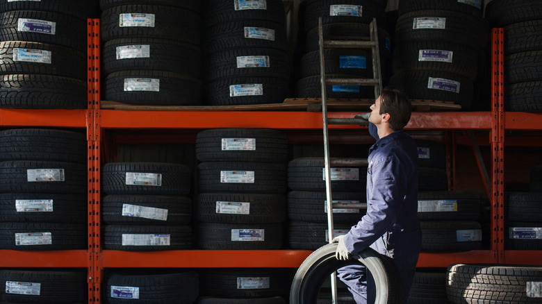Mechanic standing on a ladder, leaning against a tire rack