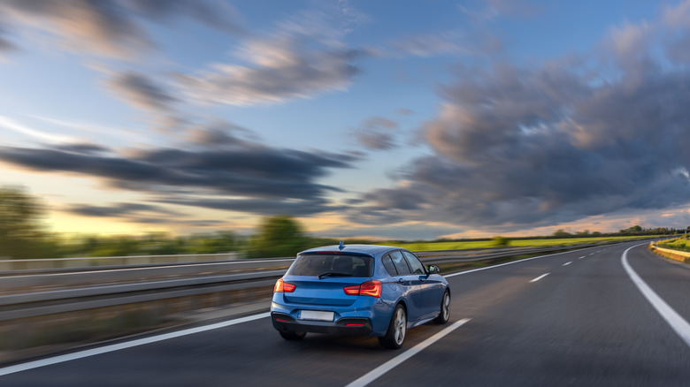 A blue car driving on a freeway in the evening