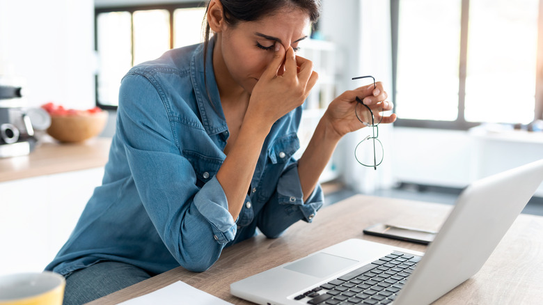 Frustrated person pinching the bridge of their nose in front of a laptop