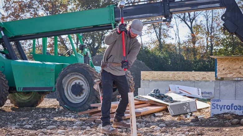A worker driving a post into the ground with Milwaukee 10-pound sledge hammer.