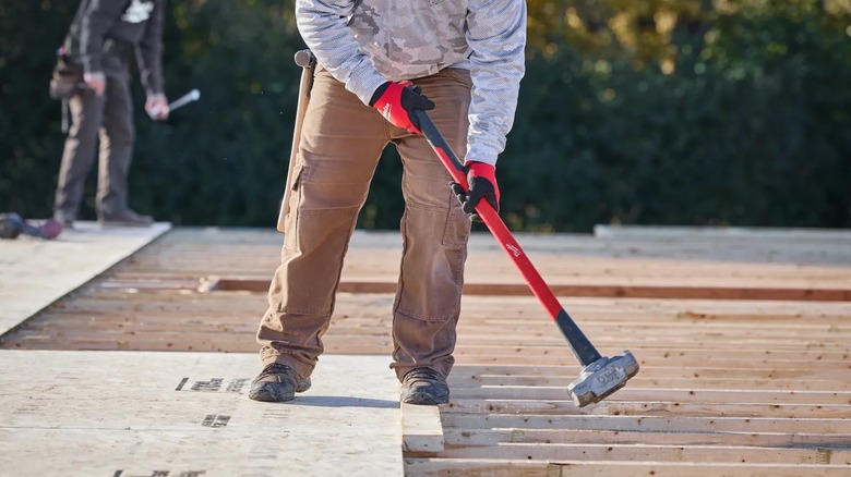 A worker laying OSB sheets with a Milwaukee 8-pound sledge hammer.