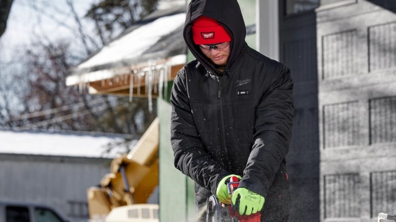 Man cutting wood in Milwaukee jacket in the snow