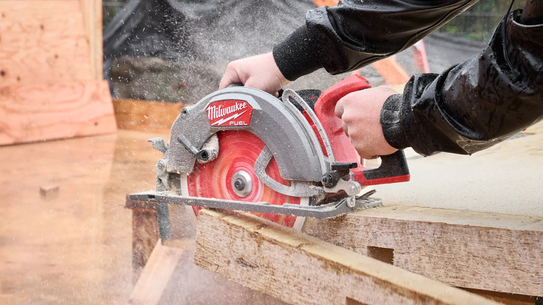 worker using a Milwaukee M18 10-1/4″ Rear Handle Circular Saw to cut one side off a wood block