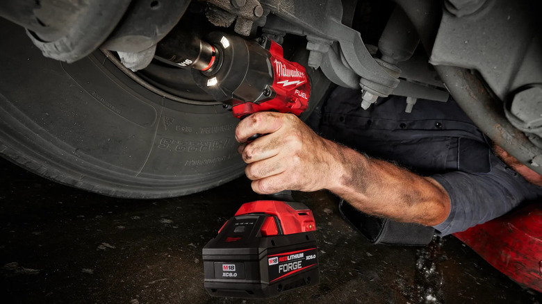 A worker using a Milwaukee M18 Fuel Impact wrench on a car.