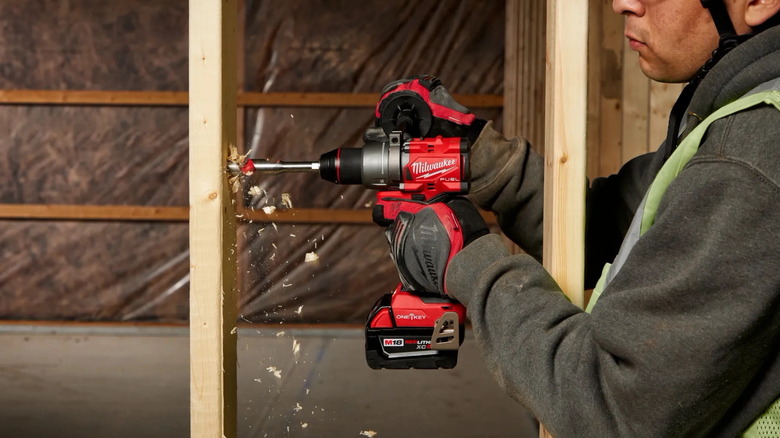 a man using a Milwaukee M18 Fuel half-inch hammer drill/driver on a wood beam