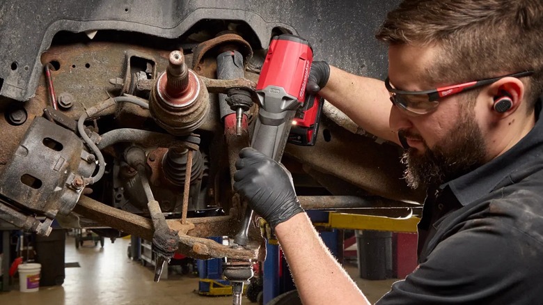 A person using a Milwaukee Striker on a vehicle suspension ball joint.