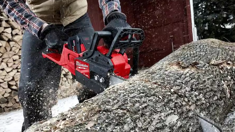 A person using a Milwaukee chainsaw on a log