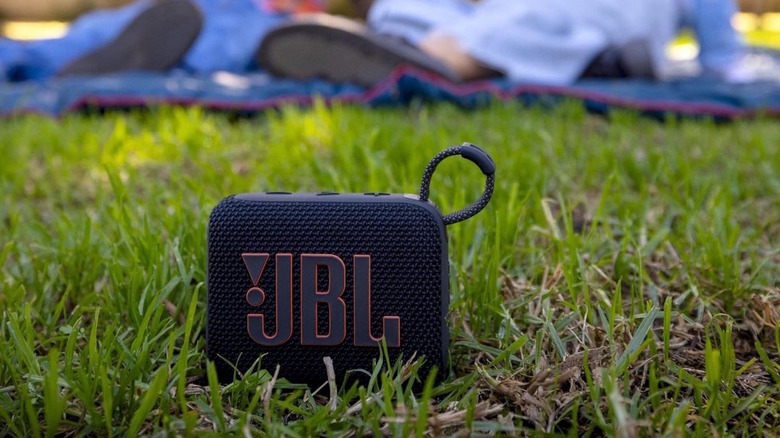 JBL Go 4 Speaker sitting on the grass with people behind it