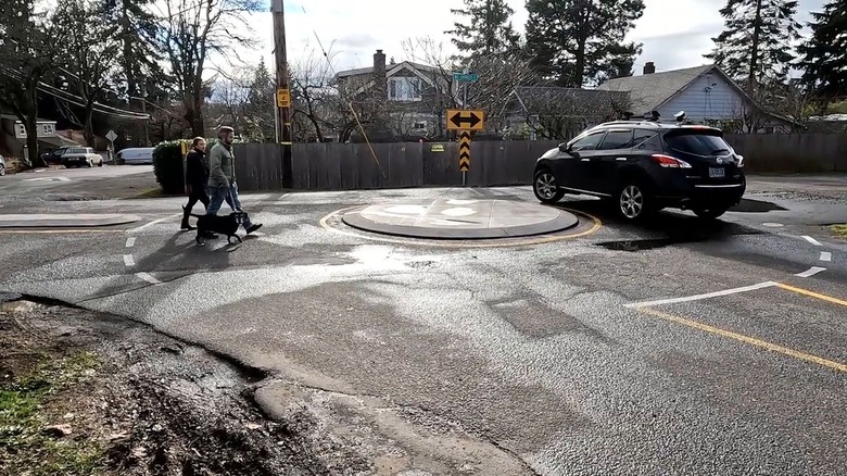 Car and pedestrians walking dog circle a mini roundabout