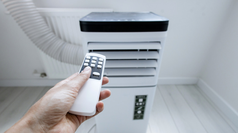 Hand adjusts portable air conditioner unit with remote