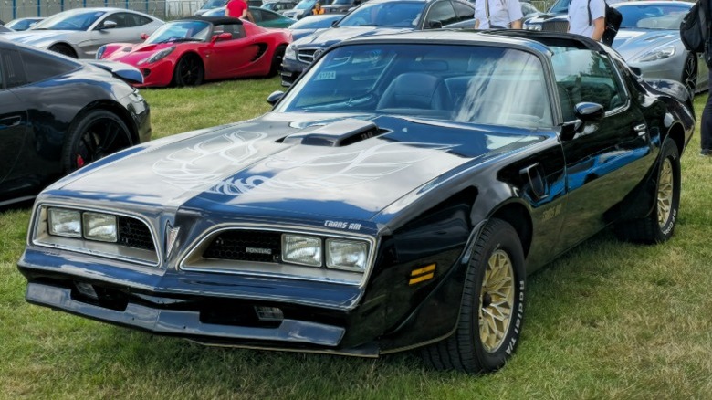 Black and gold Pontiac Firebird Trans Am parked on grass at a car show.