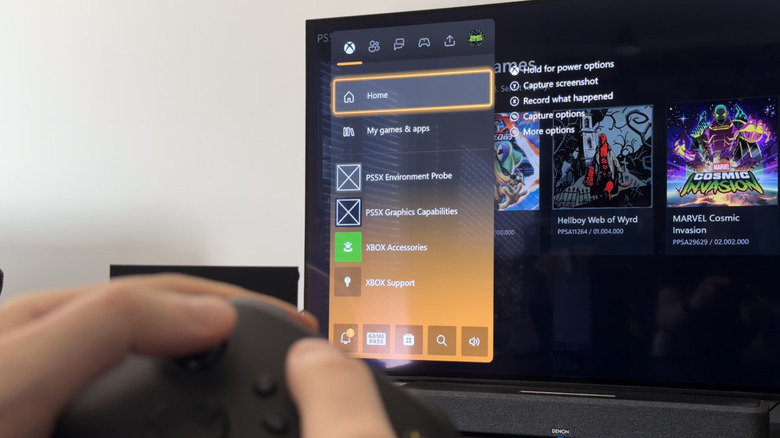 A hand holding a black Xbox controller in front of a TV, which shows PS5X in Xbox's menu