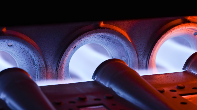 A close up of a gas furnace burner being ignited, showing a blue flame
