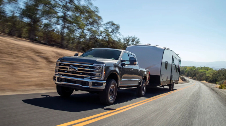 A Ford F-Series truck towing a trailer down a country road in the hills.