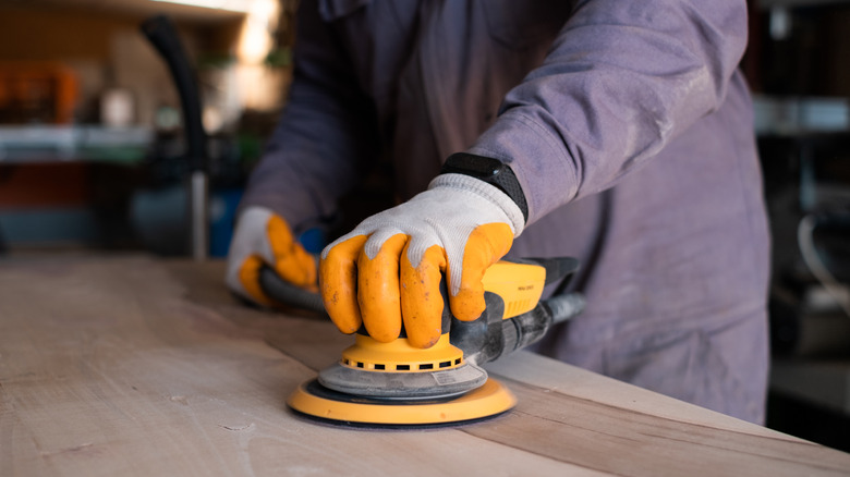 A person running a sander across unfinished wood