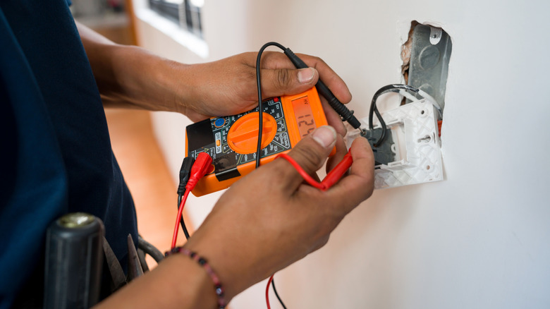 A person measuring the voltage in a socket with a multimeter
