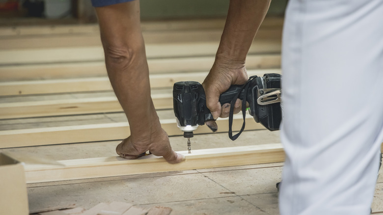 A person using an impact driver on a row of wooden planks