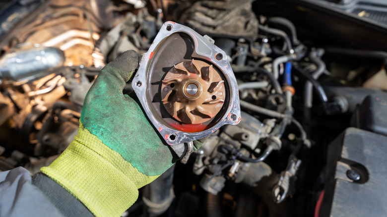 A mechanic holds a used car water pump removed from the engine