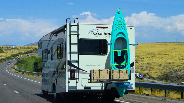 A rear view of a Coachmen RV with storage boxes and a kayak strapped to the back