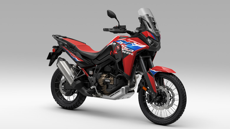 A red and black 2024 Honda Africa Twin equipped with the dual clutch transmission, parked against a studio white backdrop.