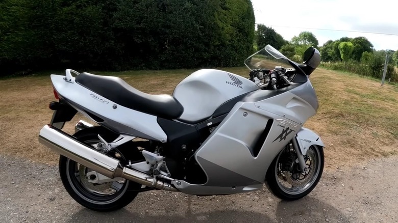 A silver-gray 2005 Honda CBR1100XX Super Blackbird parked on a small dirt road with grass and trees in the back.