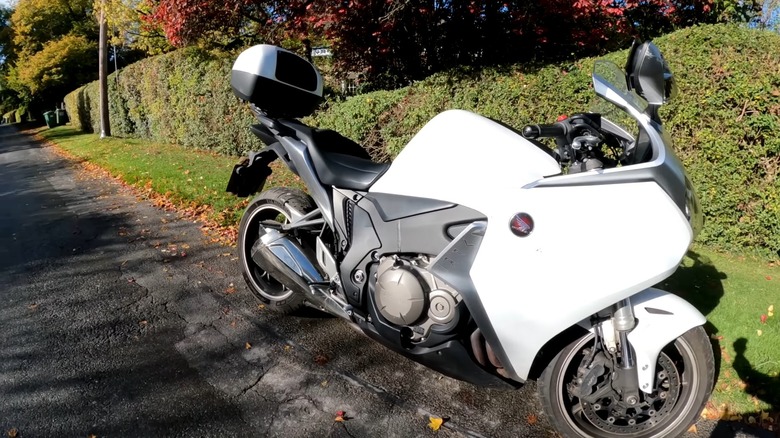 A 2011 Honda VFR1200F Interceptor in white next to a hedge, parked at the side of an internal country road.