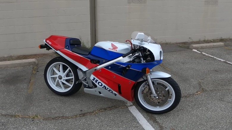A race spec Honda VFR750R Interceptor, specifically the RC30 homologation model standing outside a building, finished in red, white, and blue.