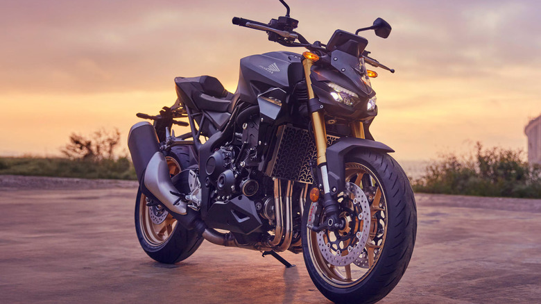 A steel gray Honda CB1000R Hornet motorbike standing on a paved surface, with the setting sun in the background.